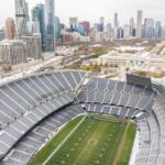 Aerial view of a large football stadium with snow, a green field, and a city skyline in the background.