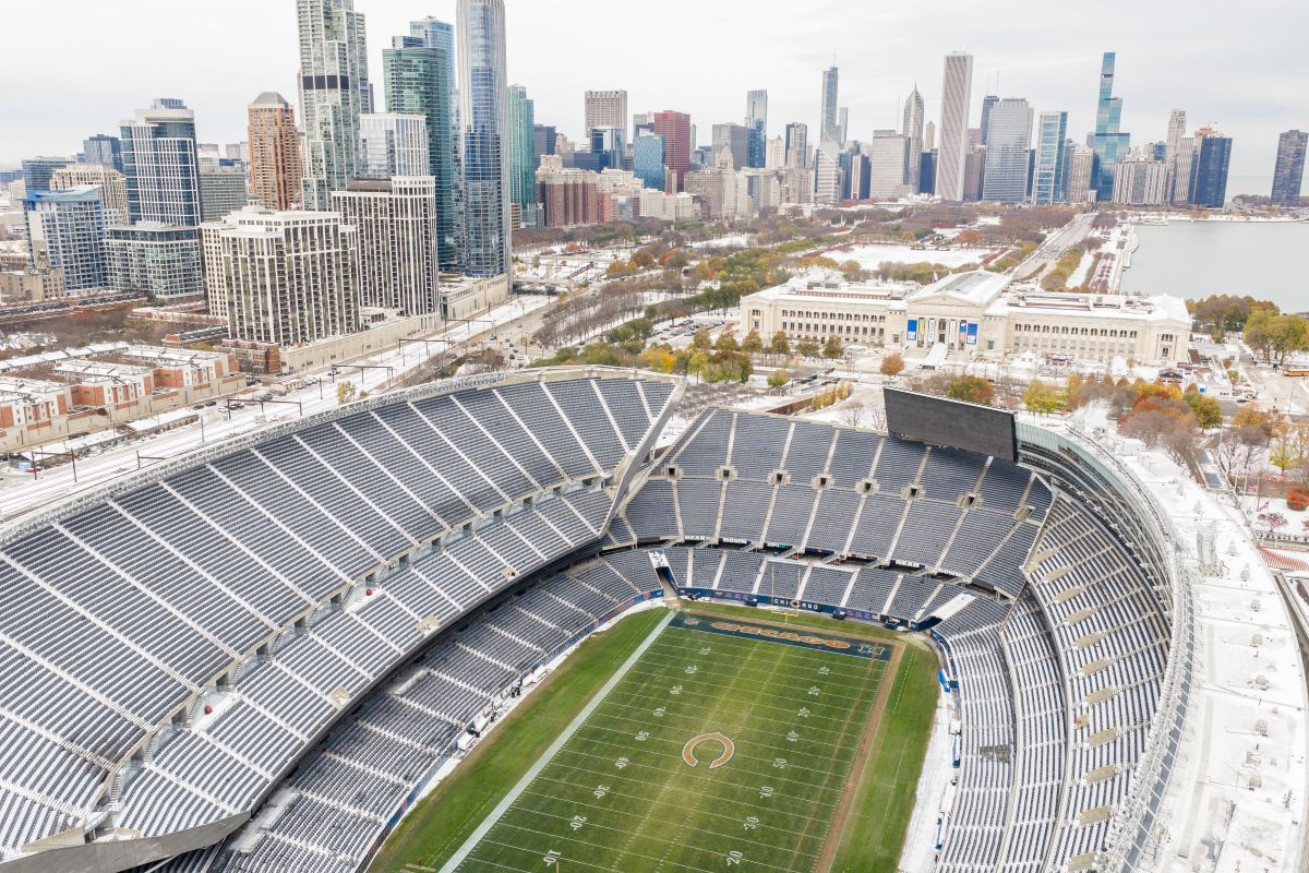 Aerial view of a large football stadium with snow, a green field, and a city skyline in the background.