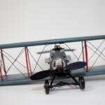 Front-facing view of a small gray biplane model with a black propeller and red struts on a light surface.