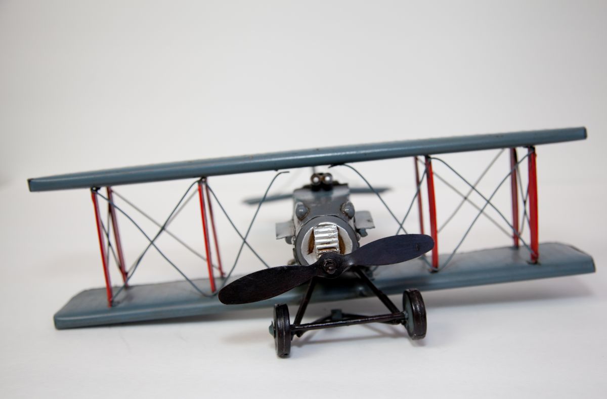 Front-facing view of a small gray biplane model with a black propeller and red struts on a light surface.