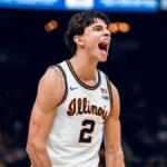 Illinois player wearing number 2 on white jersey yells with mouth open on the basketball court, opponent in yellow number 5 nearby.