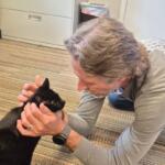 Man on the carpeted floor gently holding a black cat's head, looking at it with care (indoor setting).
