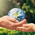 Two pairs of hands, adult and child, gently cradle a globe Earth outdoors in sunlight and grass.