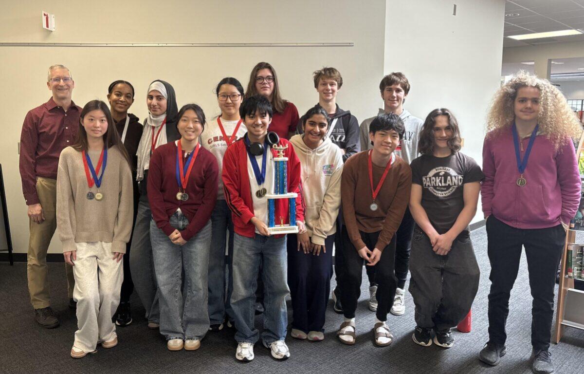 Group of diverse students in a hallway, wearing medals, posing with a tall trophy.
