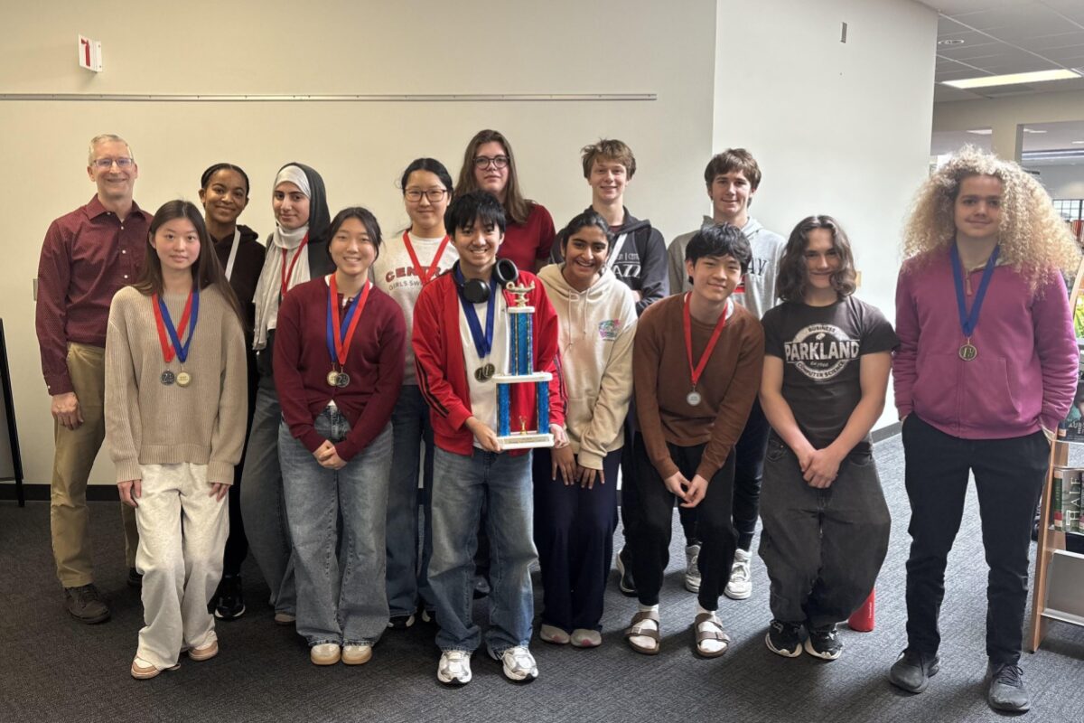 Group of diverse students in a hallway, wearing medals, posing with a tall trophy.