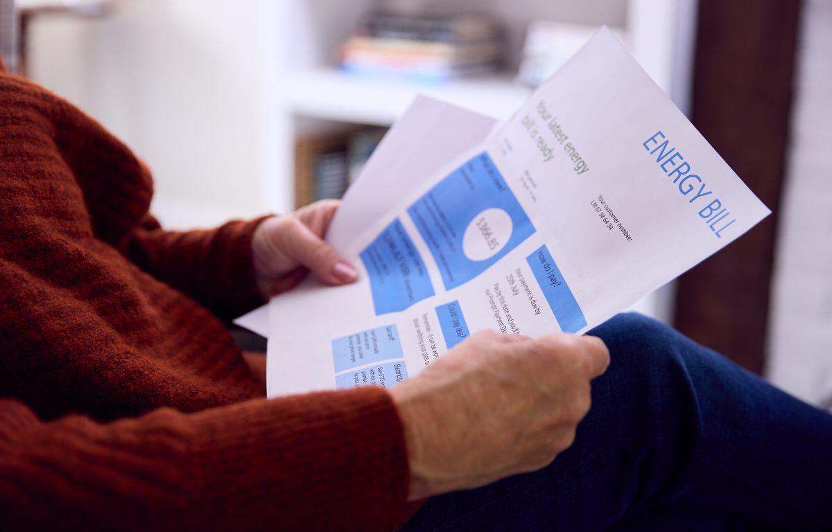 Person in a red sweater sits reading an energy bill with blue charts at home.