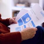 Person in a red sweater sits reading an energy bill with blue charts at home.