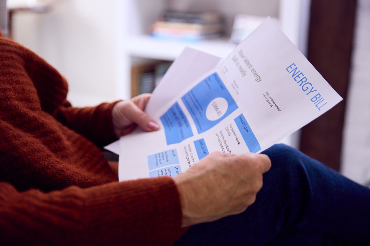 Person in a red sweater sits reading an energy bill with blue charts at home.