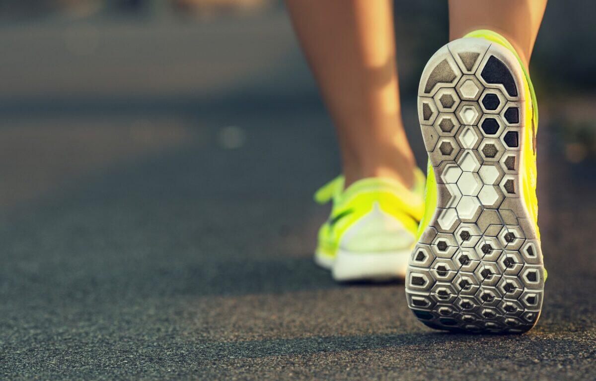 Back view of a person wearing bright yellow running shoes, stepping on a paved road in a stride gesture.