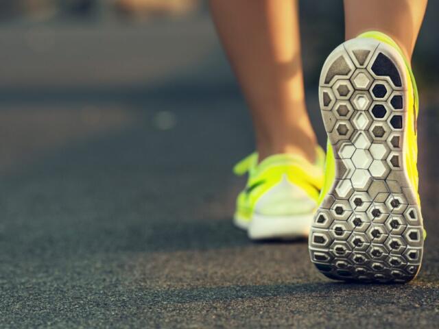 Back view of a person wearing bright yellow running shoes, stepping on a paved road in a stride gesture.