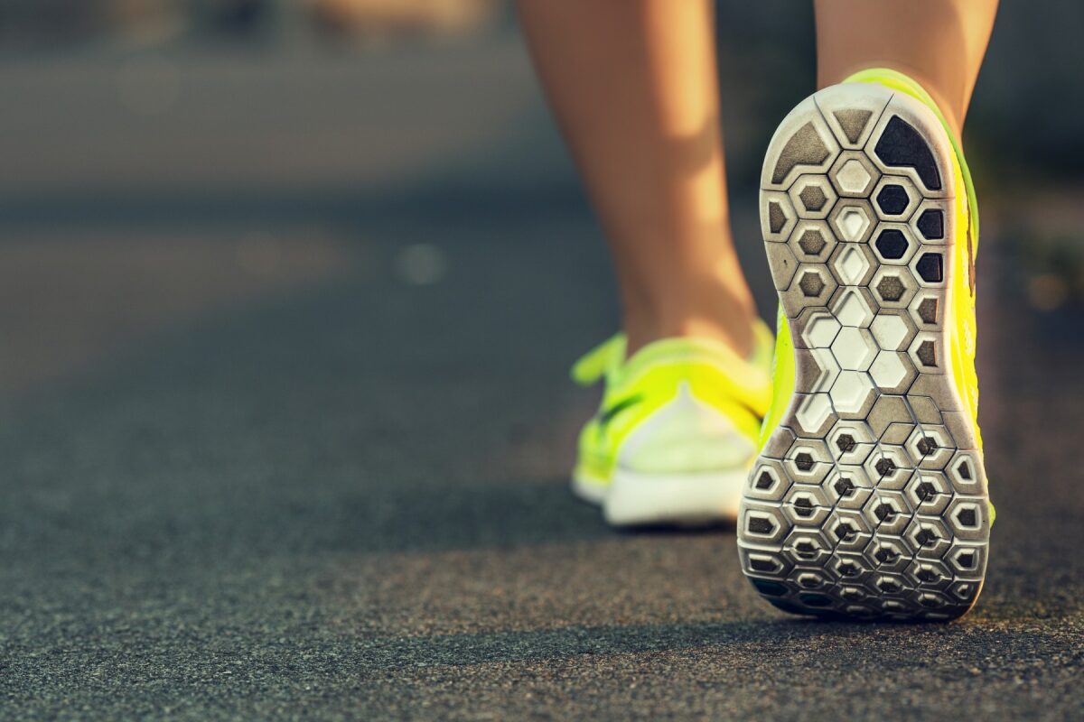 Back view of a person wearing bright yellow running shoes, stepping on a paved road in a stride gesture.