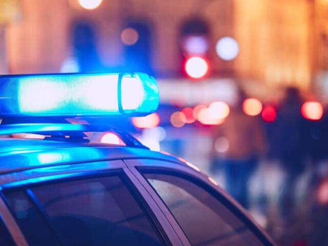 Blue police car light bar flashing at night, foreground in focus and city street blurred in the background (emergency scene).