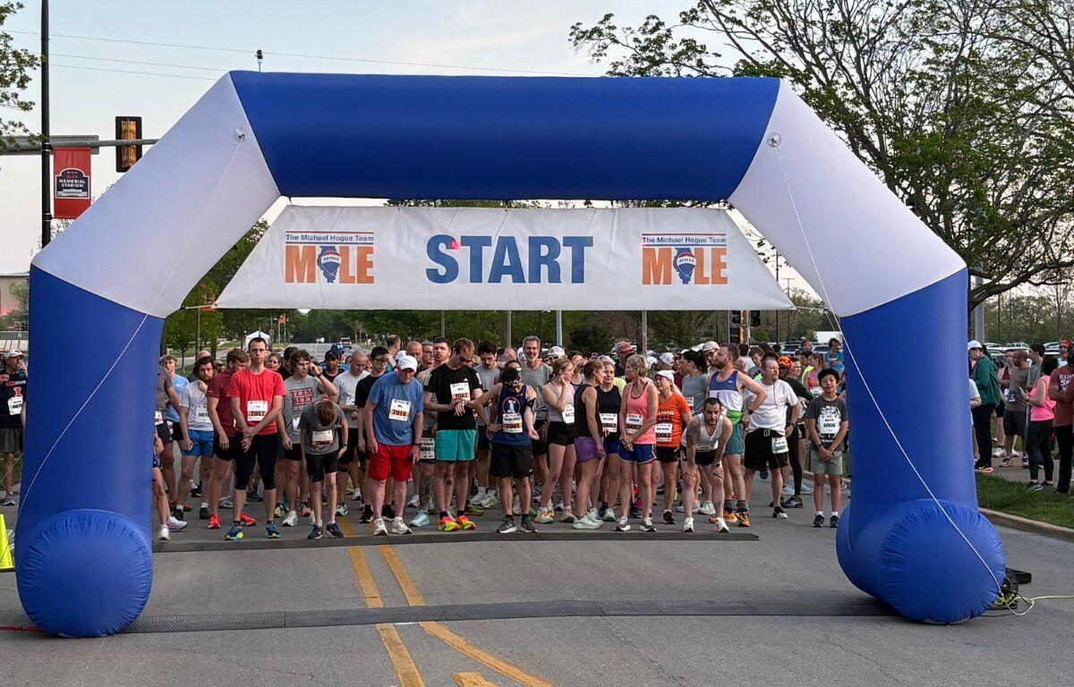 Runners lined up at the start under a blue inflatable arch with a 'START' banner across, ready for a race.