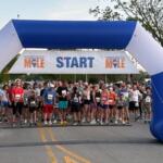 Runners lined up at the start under a blue inflatable arch with a 'START' banner across, ready for a race.