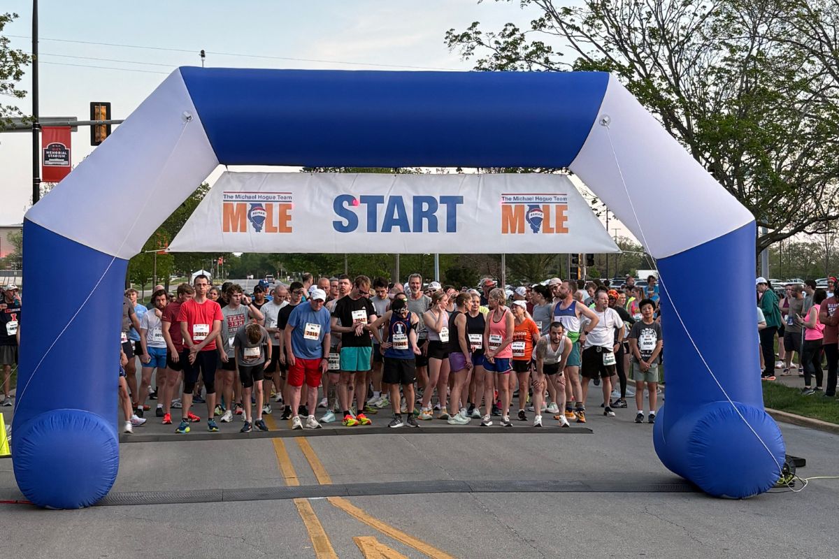 Runners lined up at the start under a blue inflatable arch with a 'START' banner across, ready for a race.