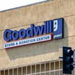 Goodwill Store & Donation Center sign on a beige wall with the blue goodwill logo to the right and a traffic light in the foreground.