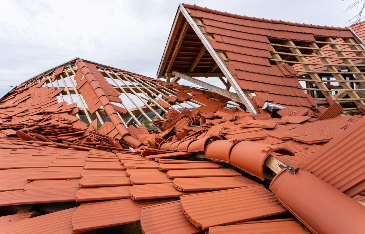Collapsed red-tile roof with wooden framing exposed, debris scattered across the structure after damage.