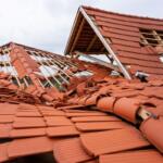 Collapsed red-tile roof with wooden framing exposed, debris scattered across the structure after damage.