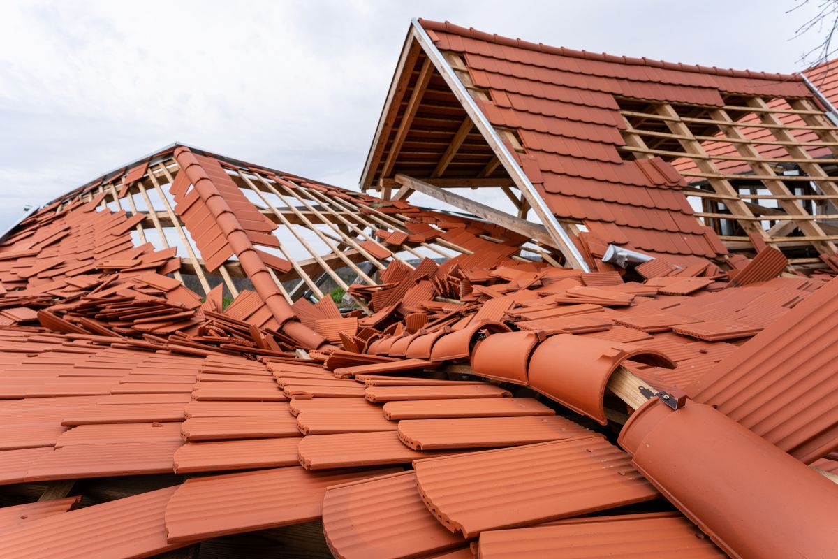 Collapsed red-tile roof with wooden framing exposed, debris scattered across the structure after damage.