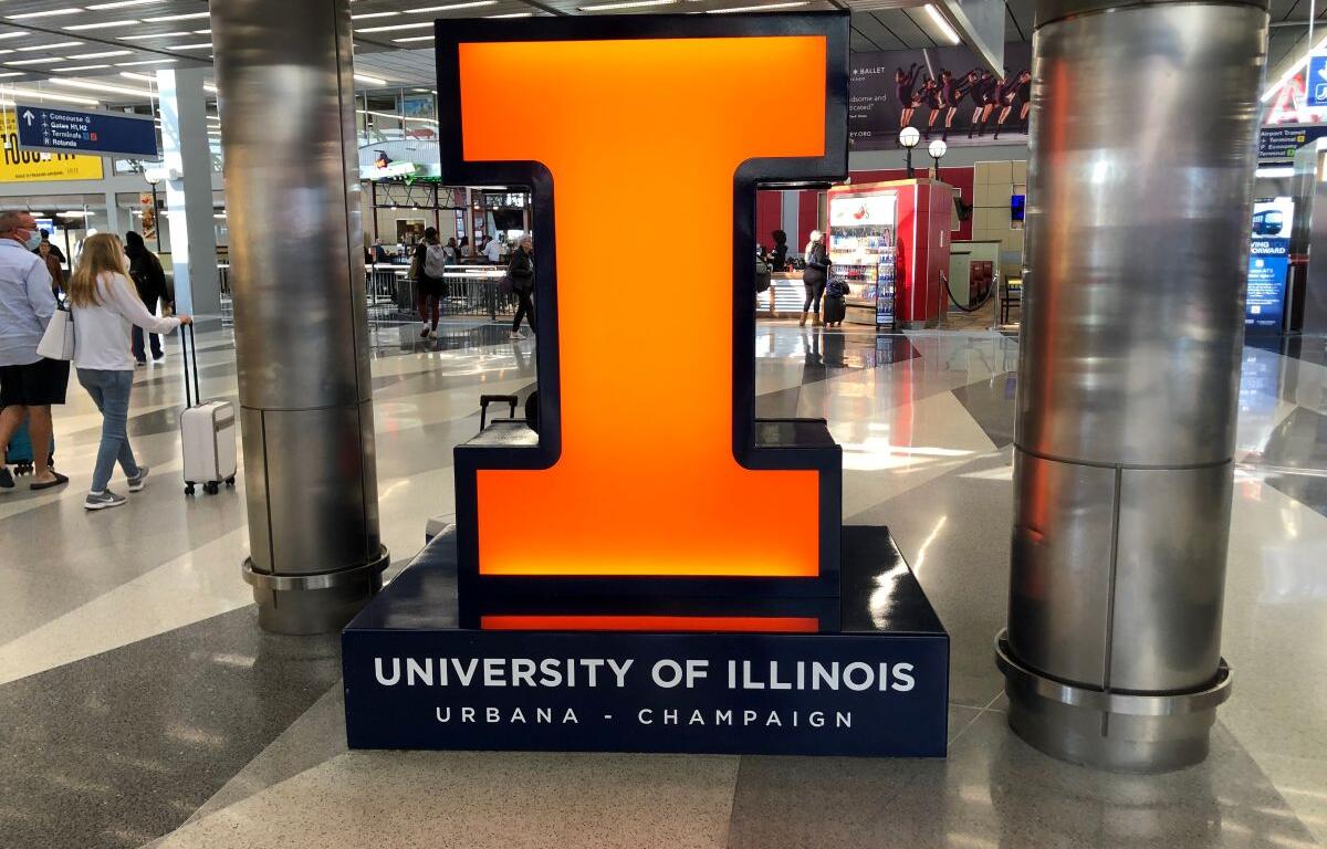 Large glowing orange numeral 1 on a dark base that says University of Illinois Urbana-Champaign in an airport terminal.