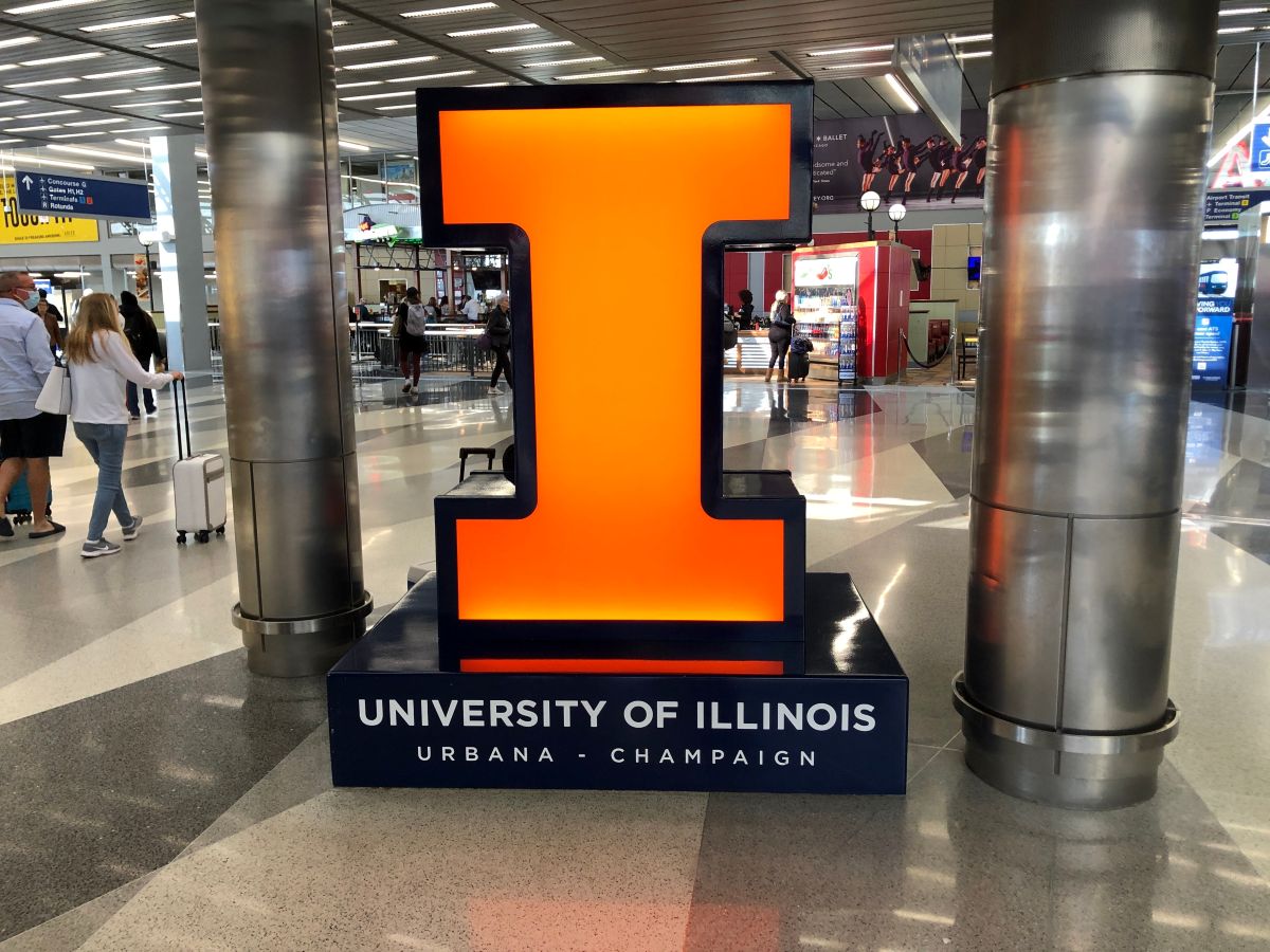 Large glowing orange numeral 1 on a dark base that says University of Illinois Urbana-Champaign in an airport terminal.