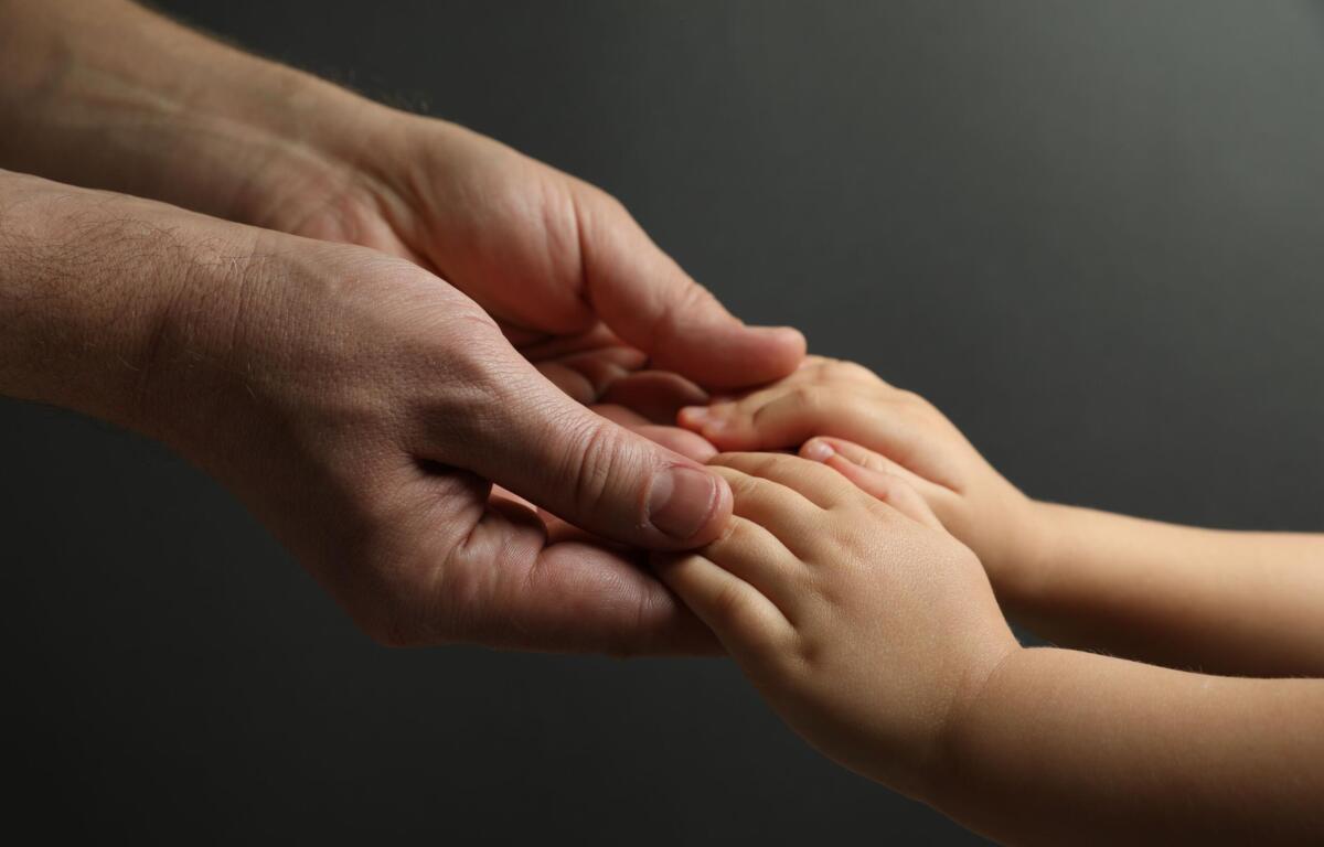 Adult hand gently cradles a baby's small hand, conveying care and connection against a dark background.