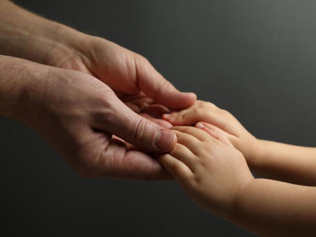 Adult hand gently cradles a baby's small hand, conveying care and connection against a dark background.
