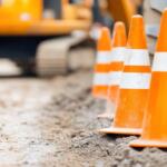 Row of orange and white safety cones on a muddy construction site with blurred heavy machinery in the background