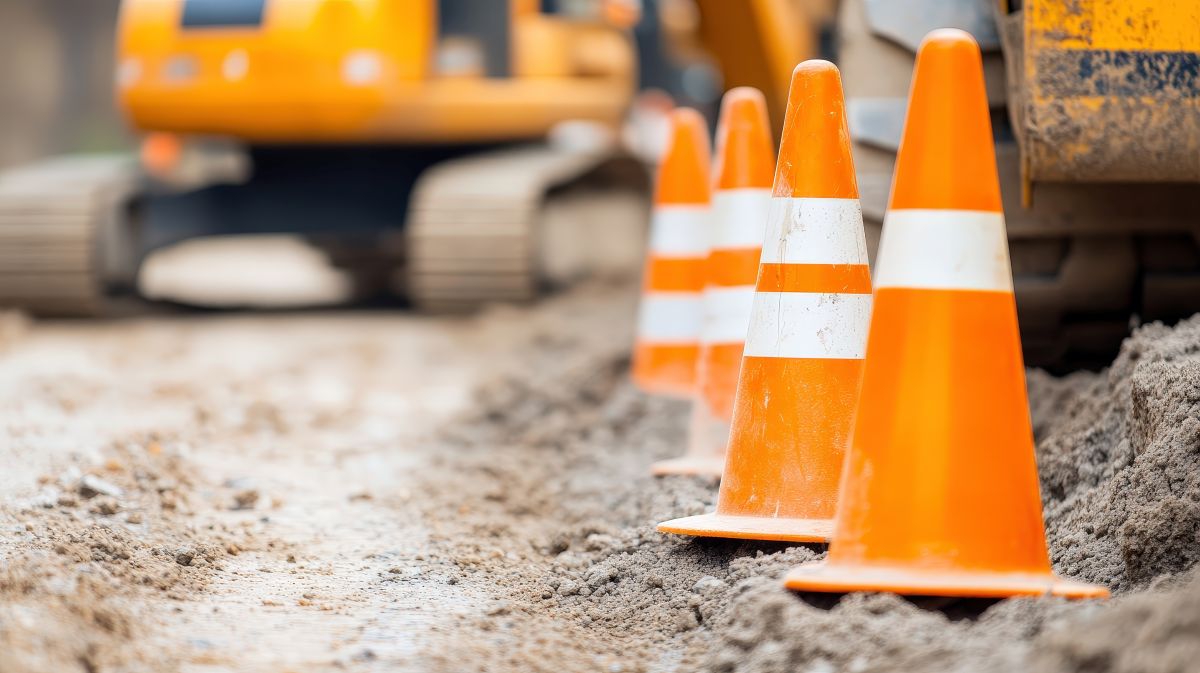 Row of orange and white safety cones on a muddy construction site with blurred heavy machinery in the background