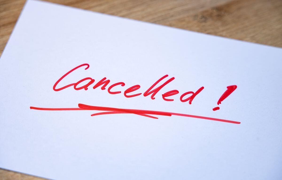 White paper with red handwritten 'Cancelled!' and an underline on a wooden surface.