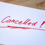 White paper with red handwritten 'Cancelled!' and an underline on a wooden surface.