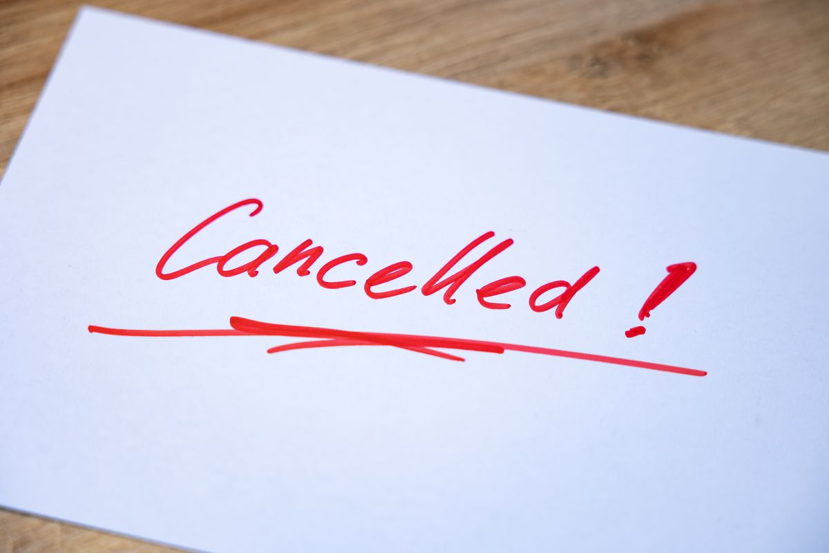 White paper with red handwritten 'Cancelled!' and an underline on a wooden surface.