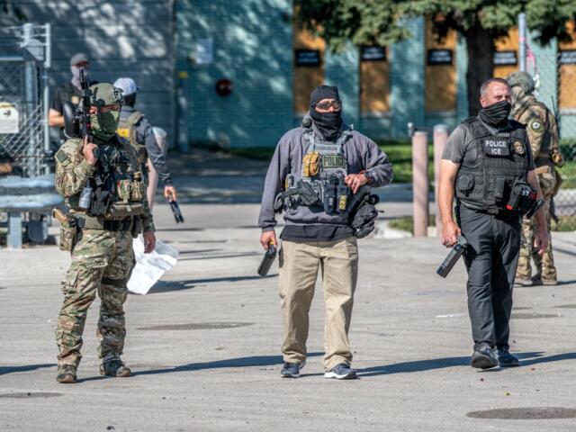 Tactical police team in armor and masks stand outdoors with weapons ready.