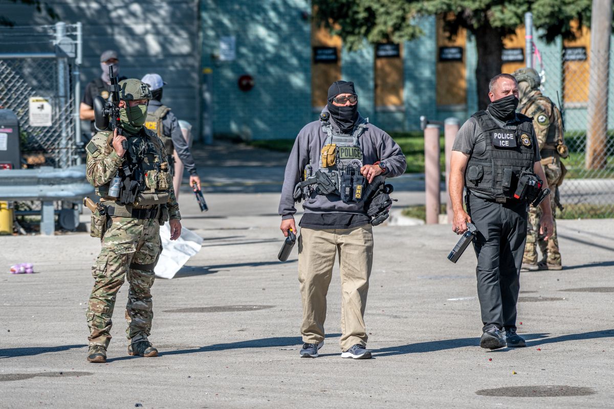 Tactical police team in armor and masks stand outdoors with weapons ready.