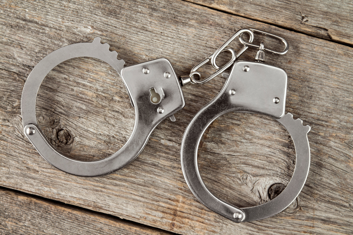 Pair of metal handcuffs on a weathered wooden surface.
