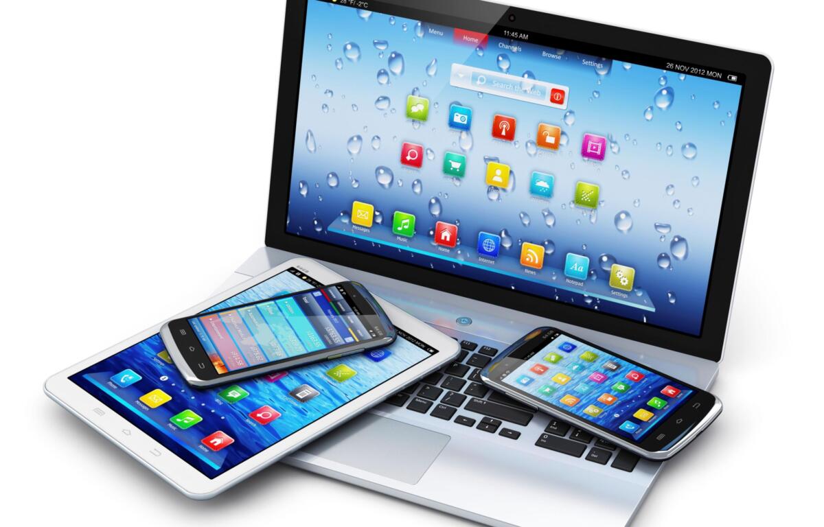 Angled group of tablets and smartphones resting on a laptop keyboard, screens filled with colorful app icons.