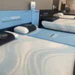 Row of Tempur-Pedic Act ive Breeze beds in a showroom with pillows and blue protective sheets on each bed.