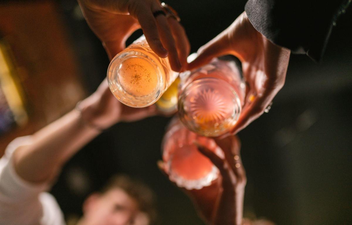 People raise pink cocktails in a toast, seen from above during a celebration.