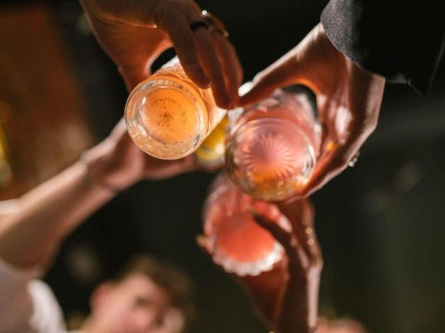 People raise pink cocktails in a toast, seen from above during a celebration.