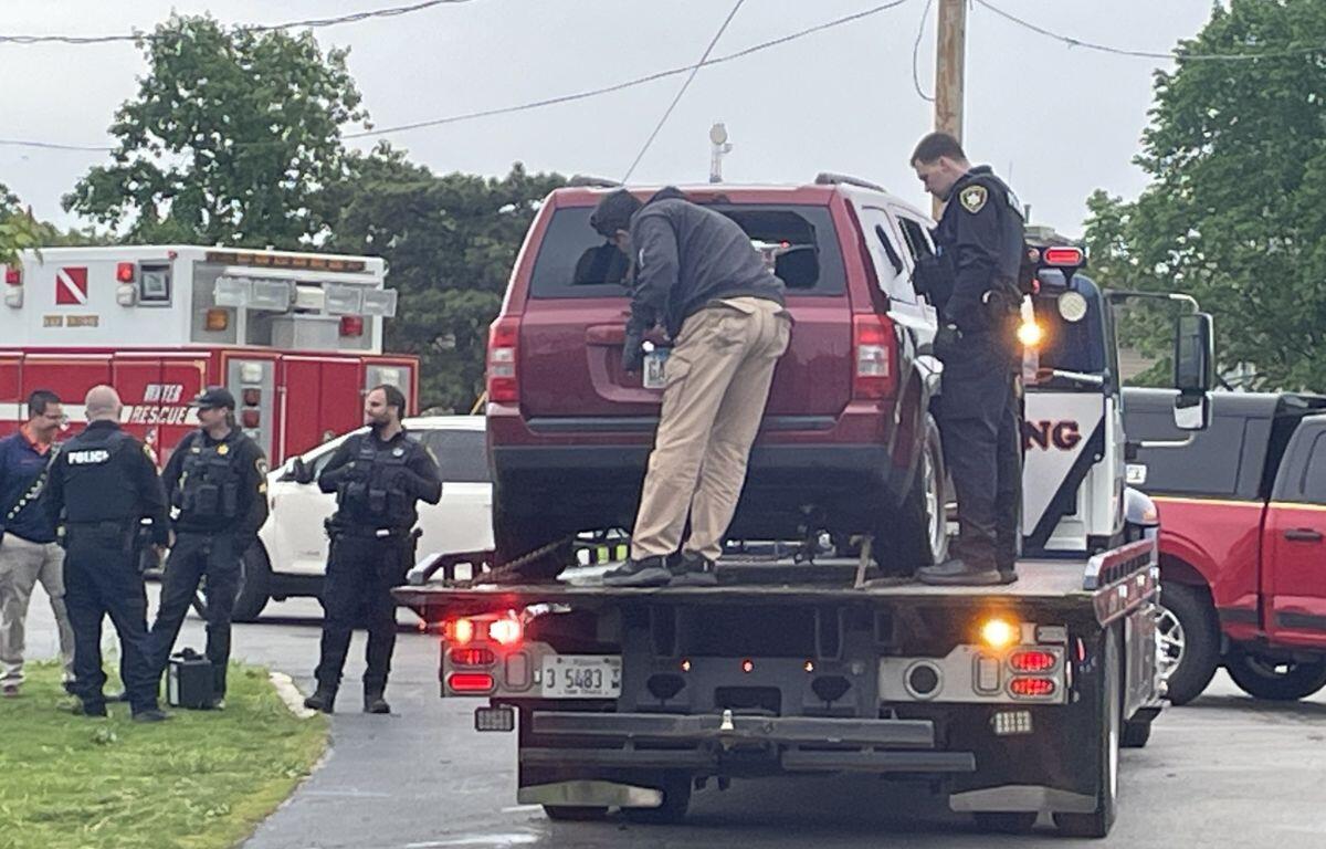 Tow truck carrying a red SUV with officers standing nearby, some in police vests, at a daytime roadside incident.