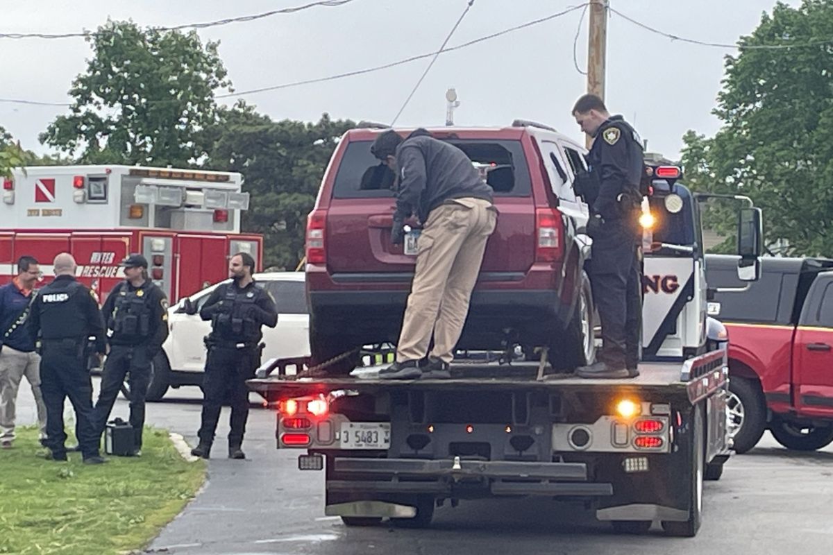 Tow truck carrying a red SUV with officers standing nearby, some in police vests, at a daytime roadside incident.