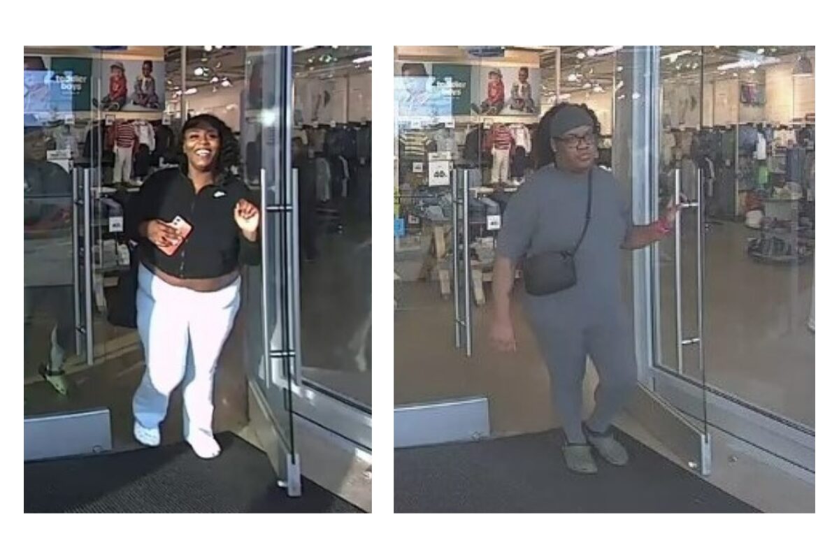 Two women exit a clothing store through glass doors; left woman smiles, wearing a black top and white pants, holding a card. Right woman in gray outfit with a black crossbody bag exits beside her.