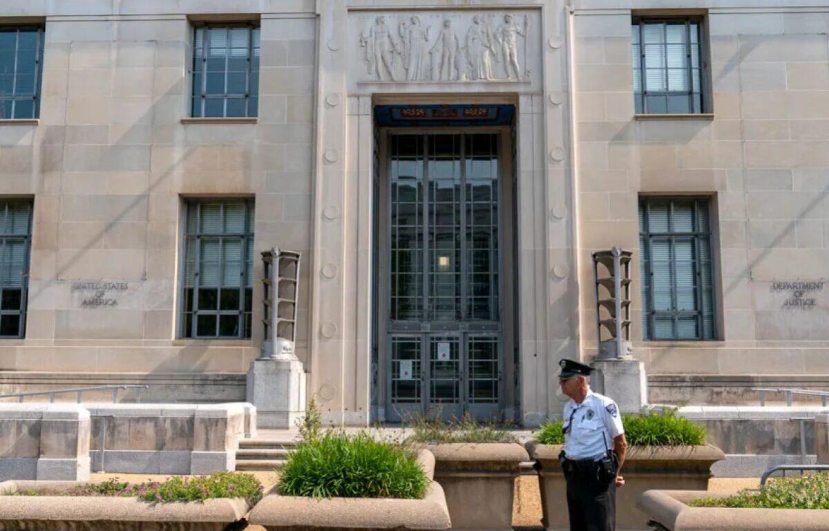 Front entrance of a government building with a security guard standing near planters and steps.