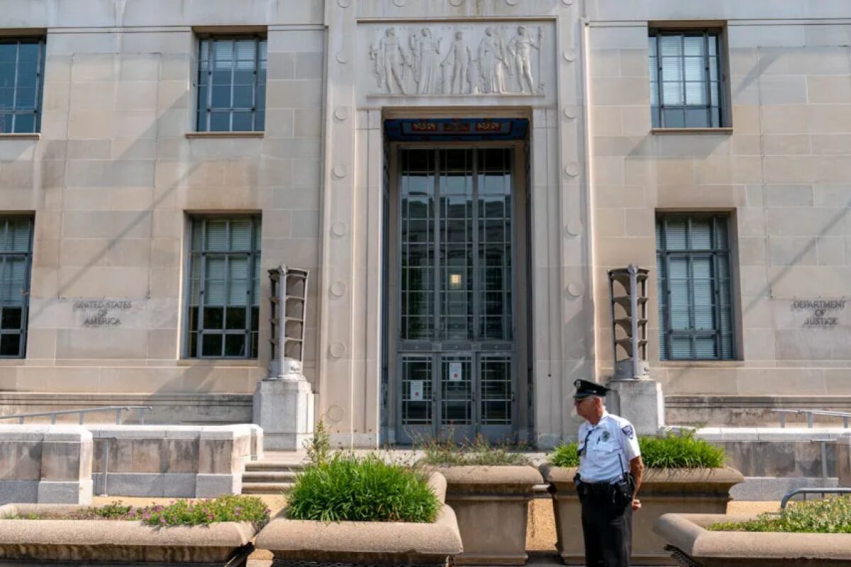 Front entrance of a government building with a security guard standing near planters and steps.