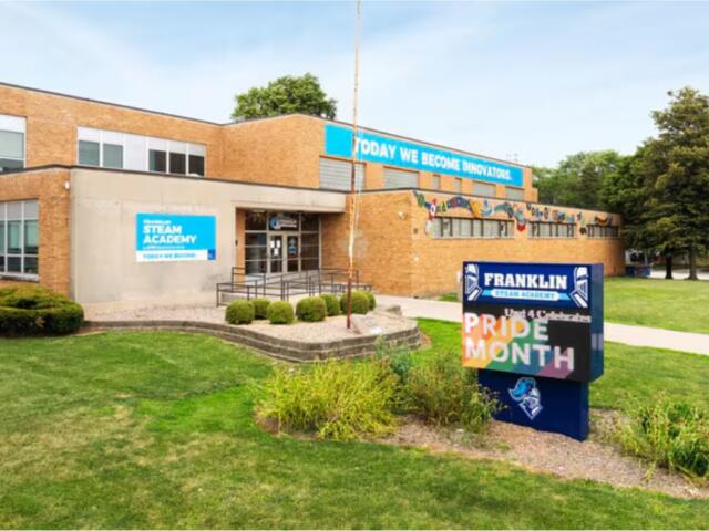 Exterior view of Franklin STEAM Academy, a brick school building with Pride Month signage in the front yard display.