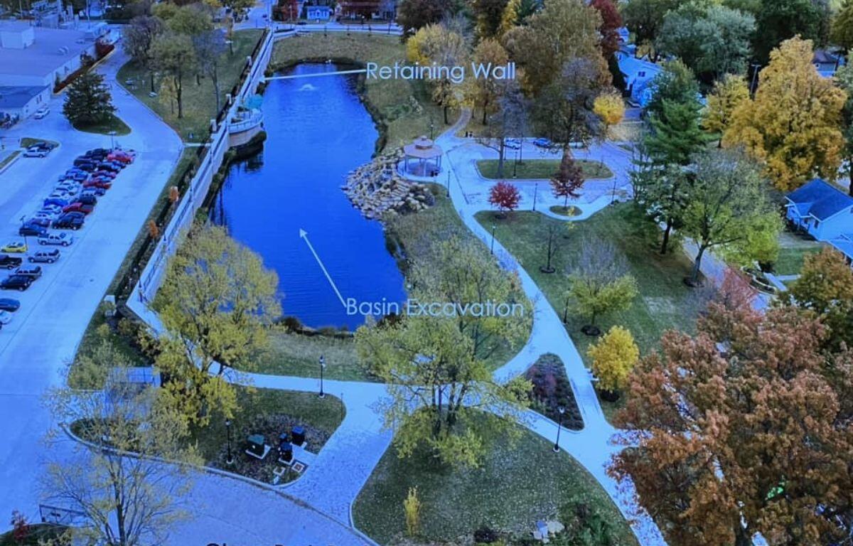 Aerial view of a park with a kidney-shaped basin labeled 'Basin Excavation' and a raised 'Retaining Wall' along the water, surrounded by trees and pathways.