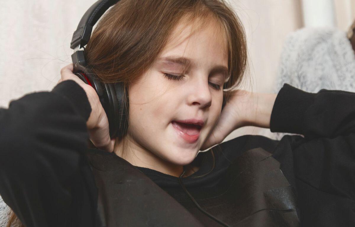 Young girl wearing over-ear headphones with eyes closed, absorbed in music.