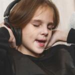 Young girl wearing over-ear headphones with eyes closed, absorbed in music.