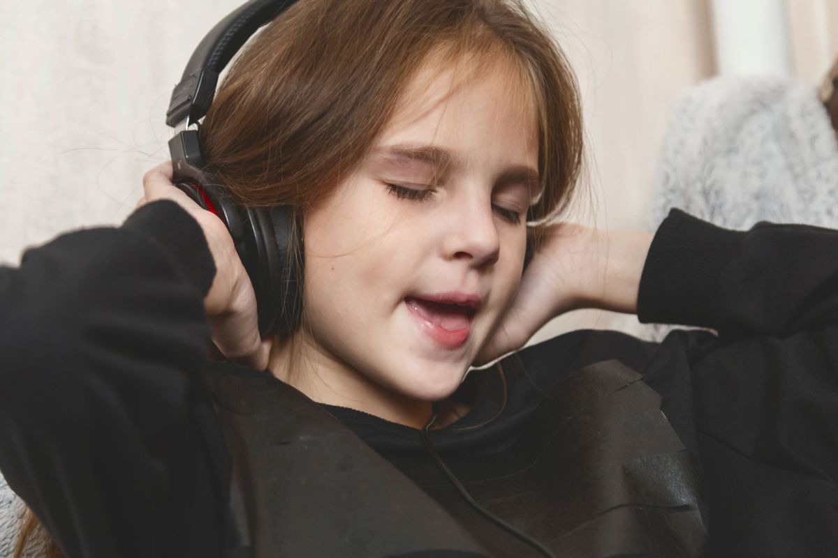 Young girl wearing over-ear headphones with eyes closed, absorbed in music.