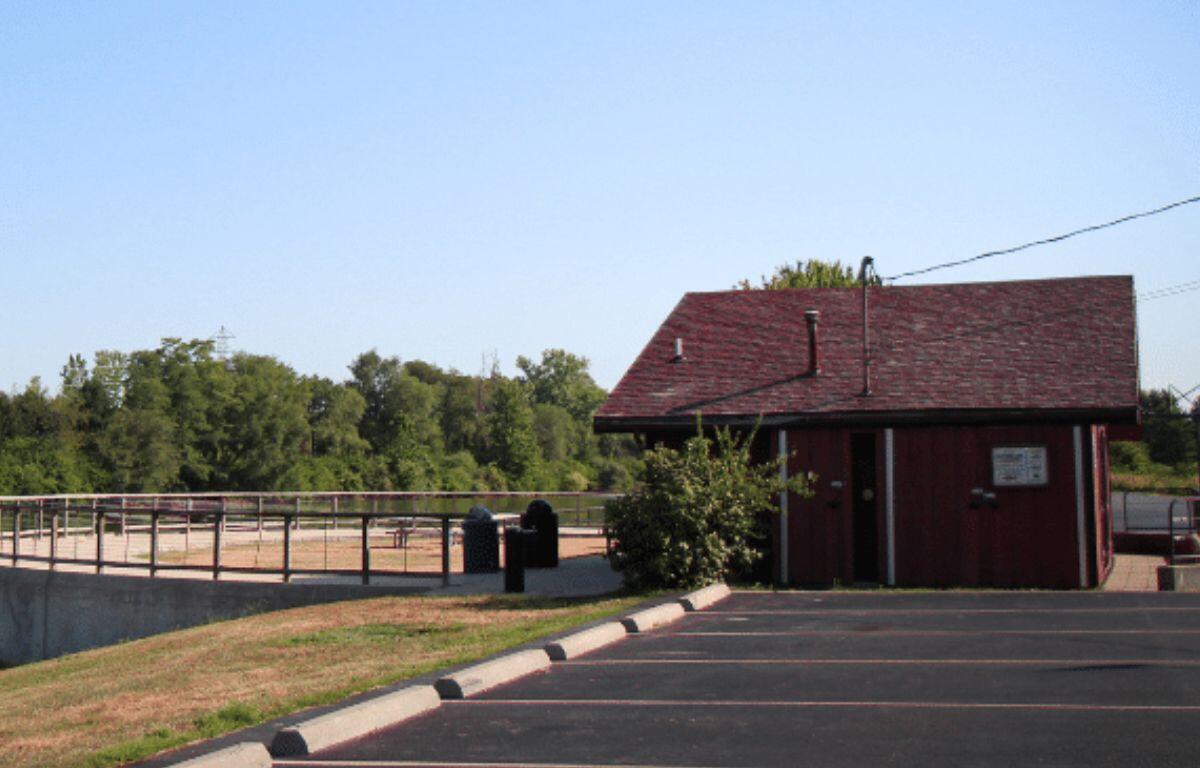 Red wooden concession-style building with a sloped roof beside a paved parking lot under a clear blue sky.